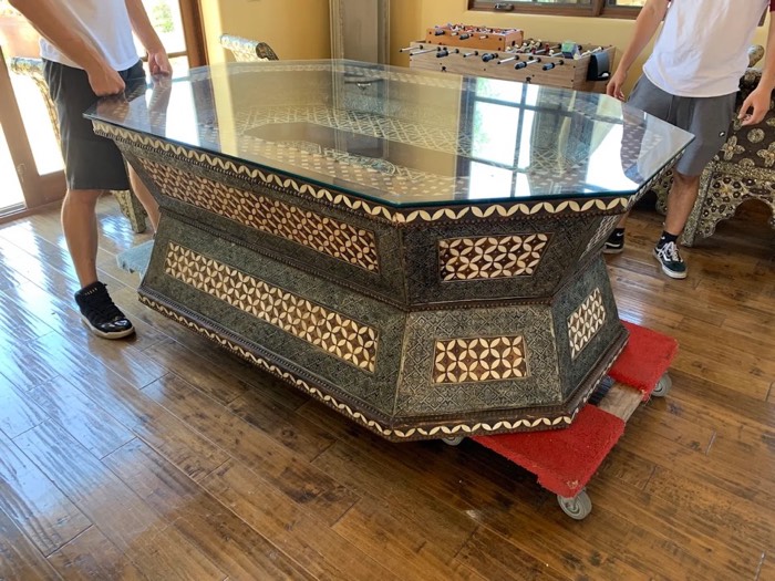 Happy Home Moovers crew moving a large ornate glass-top table with a furniture dolly